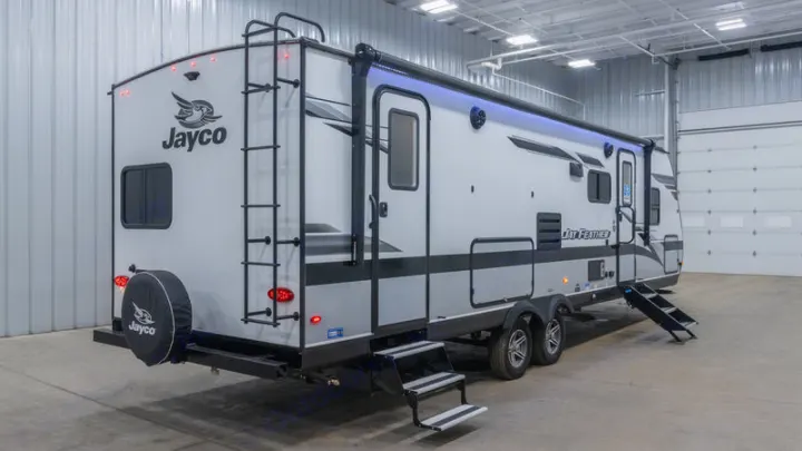 Jayco Jay Feather travel trailer, an excellent RV rental choice. Rear-side view highlights ladder, steps, blue awning light.. Jayco Jay Feather 2022