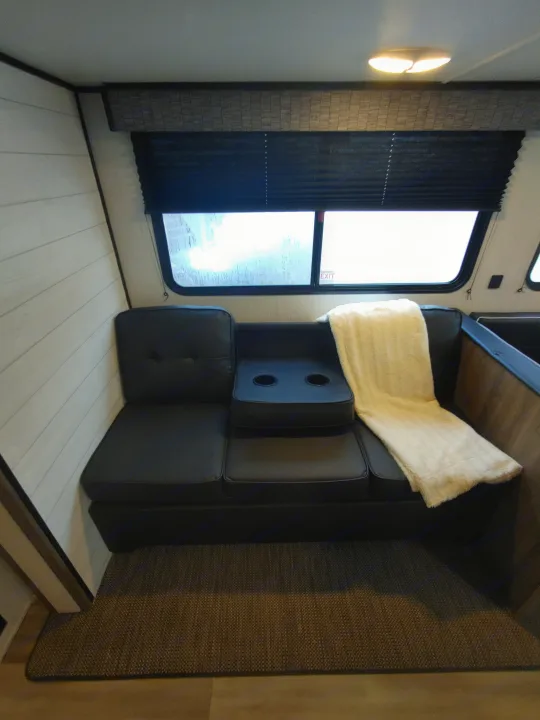 Inside an rv rental: black modular seating with cup holders, a window, light wood-look flooring, and warm wall light.. Heartland Pioneer 2022
