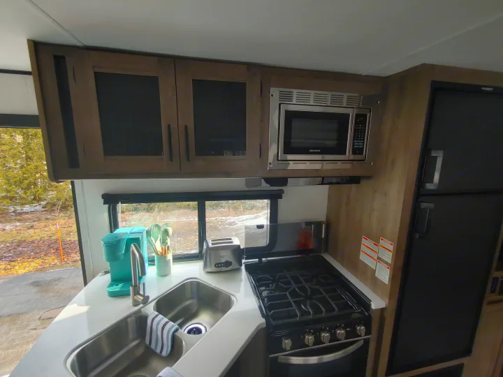 RV rental: Fully equipped kitchen featuring a microwave, stove, fridge, double sink, light wood cabinets, and outdoor scenery.. Heartland Pioneer 2022