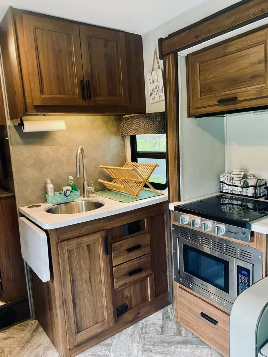 Modern RV rental kitchen with sink, stovetop, microwave, and pull-out counter, maximizing compact space.. Forest River Sunseeker 3250DSLE 2022