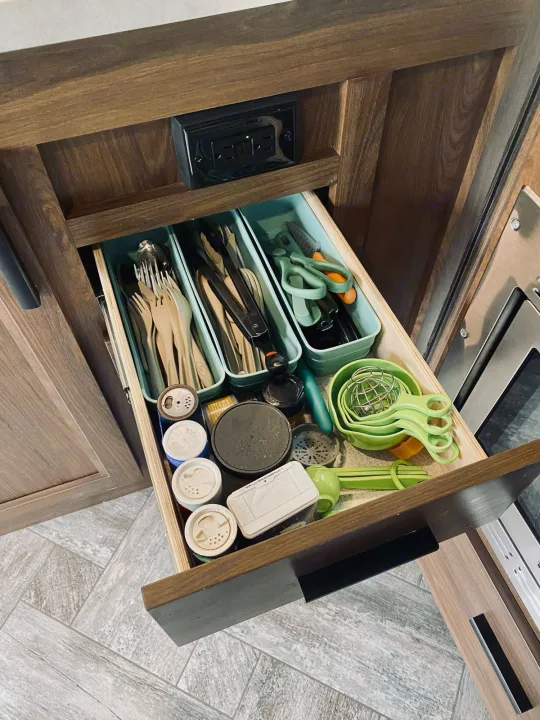 RV rental kitchen drawer, well-organized with green bins holding various utensils, measuring cups, and spice containers.. Forest River Sunseeker 3250DSLE 2022