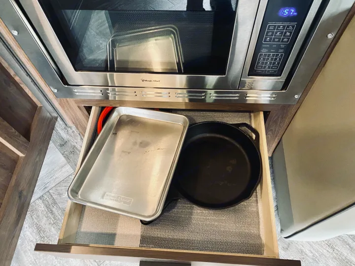 In an RV rental kitchen, a Magic Chef microwave sits above an open drawer neatly storing a baking sheet and cast iron skillet.. Forest River Sunseeker 3250DSLE 2022