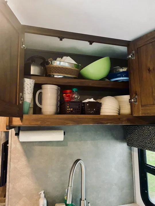 Open, organized kitchen cabinets in an RV rental, displaying dishes, kettle, and a sink with paper towels.. Forest River Sunseeker 3250DSLE 2022