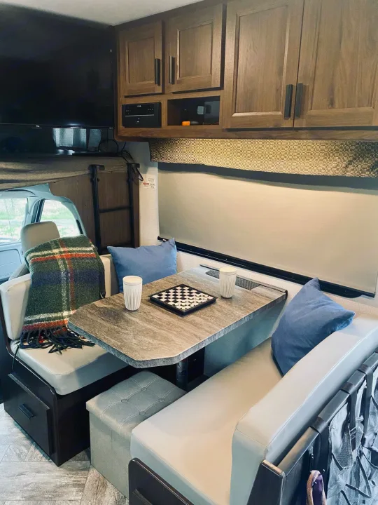 RV rental's inviting interior: dinette with checkered game, padded benches, TV, and overhead storage for comfortable travel.. Forest River Sunseeker 3250DSLE 2022