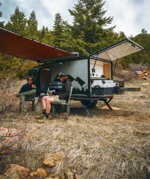 Two friends relax with an RV rental, a small camping trailer, under an awning with an outdoor kitchen in a scenic natural setting.. Other Other 2019