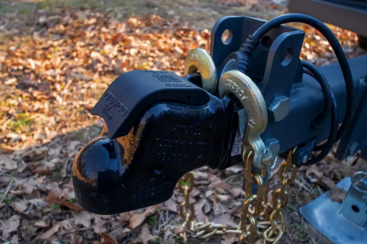 Close-up of a Demco EZ Latch trailer coupler with safety chains and electrical wiring, essential for your RV rental towing.. Campinawe Sport 2022