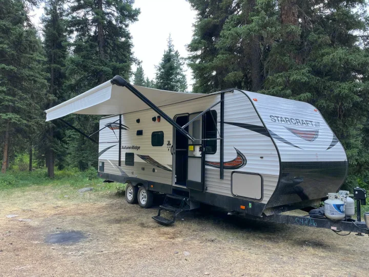 Starcraft Autumn Ridge RV rental with awning extended and steps down, nestled among tall trees.. Starcraft Autumn Ridge 2018