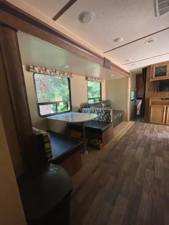 Spacious RV rental interior featuring a dinette, sofa, and windows showing trees, with wood-look flooring.. Starcraft Autumn Ridge 2018