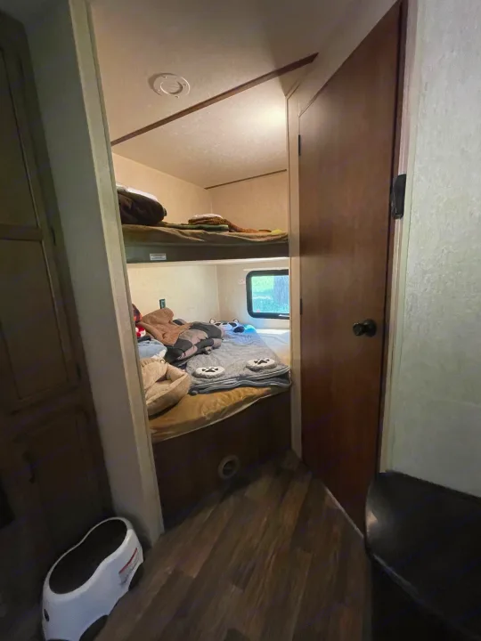 RV rental interior: a cozy, compact bunk bed area with blankets, a window, and dark wood flooring.. Starcraft Autumn Ridge 2018