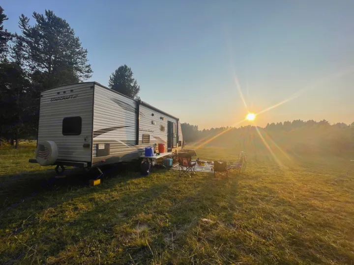 Sunrise over an RV rental, a Starcraft travel trailer set up in a lush grassy field. Ideal for camping outdoors in nature.. Starcraft Autumn Ridge 2018