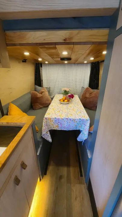 Cozy RV rental interior: a dining area with floral tablecloth, U-shaped seating, kitchenette, and warm lighting.. Mercedes-Benz Sprinter 2019