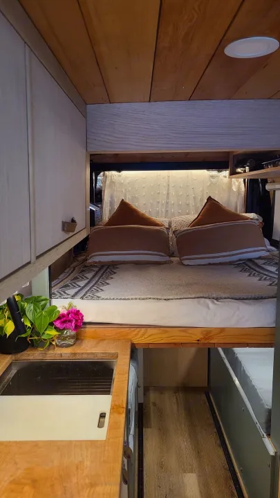 Cozy RV rental interior with wooden details, featuring a comfortable bed and compact kitchen area with a sink.. Mercedes-Benz Sprinter 2019