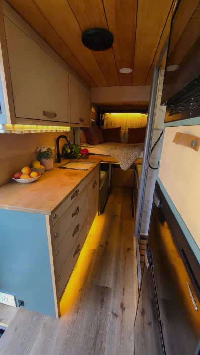 Cozy RV rental interior featuring a full kitchen, raised bed, and warm wood finishes with ambient lighting.. Mercedes-Benz Sprinter 2019