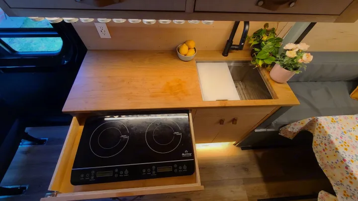 Compact RV rental kitchen features a clever pull-out induction cooktop, sink, and organized storage for efficient van life.. Mercedes-Benz Sprinter 2019