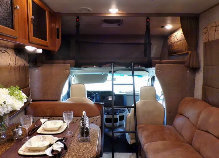 Inside a comfortable rv rental: set dining table, an over-cab bunk with safety net and ladder, and a plush sofa.. Coachmen Leprechaun 2018