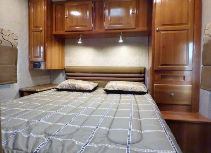 Cozy RV rental bedroom with wood cabinets, a comfy bed, and reading lights, perfect for travel.. Coachmen Leprechaun 2018