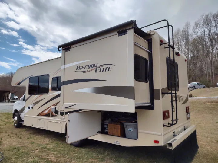 Spacious cream "Freedom Elite" RV rental with slide-out extended and storage open, parked on grass.. Thor Freedom Elite 2017