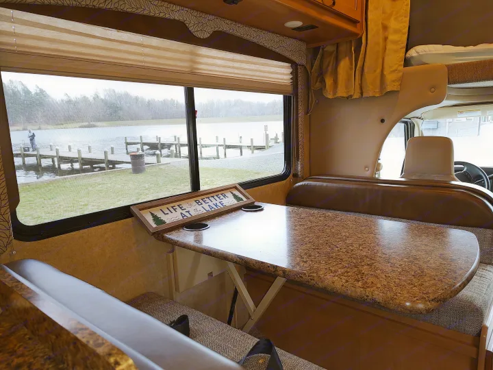 RV rental dining area with lake view: a booth, table with cup holders, and a 'LIFE is BETTER AT THE LAKE' sign.. Thor Freedom Elite 2017