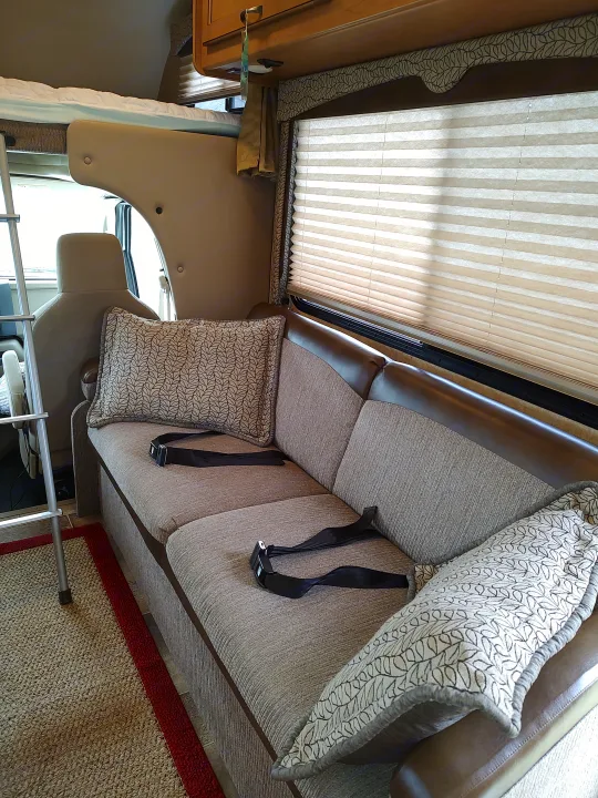 Cozy RV rental interior: a comfy sofa with seatbelts, decorative pillows, and pleated window blinds.. Thor Freedom Elite 2017