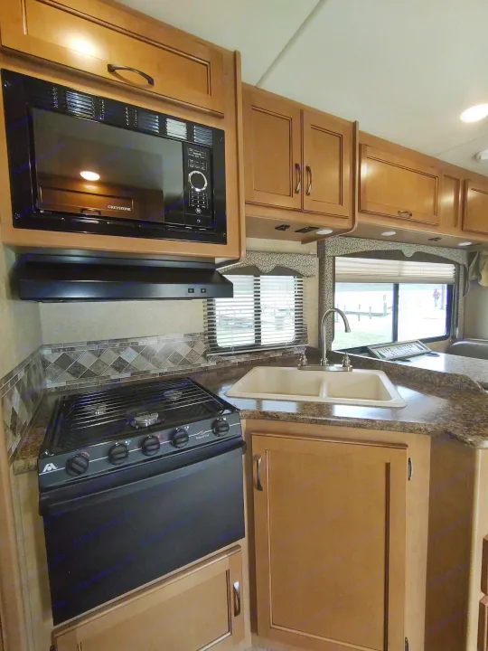 RV rental kitchen: light wood cabinets, black Greystone microwave, stove, sink, tiled backsplash & floor.. Thor Freedom Elite 2017