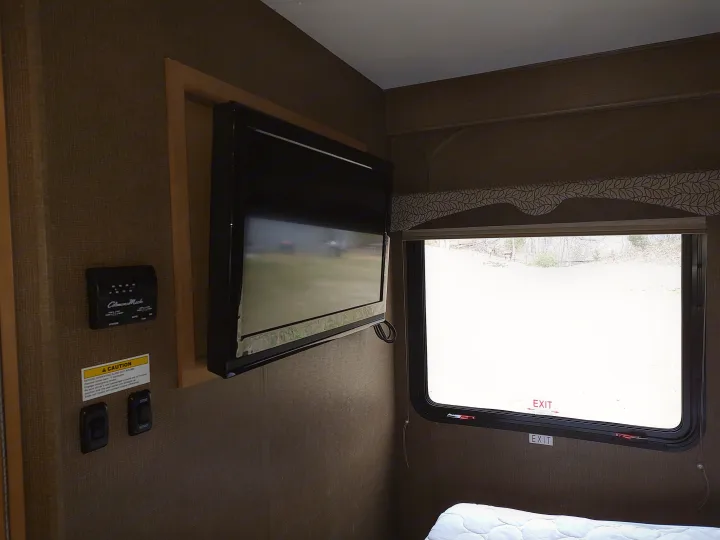 RV rental interior: TV, climate controls, and emergency exit window with outdoor view. Bed visible at bottom.. Thor Freedom Elite 2017