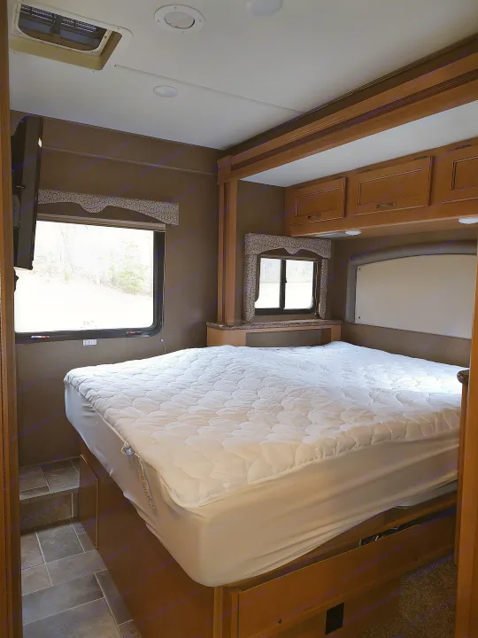Cozy RV rental bedroom with a large bed, overhead cabinets, and windows offering natural light. Perfect for travel.. Thor Freedom Elite 2017