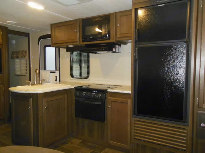 Modern RV rental kitchen featuring a sink, microwave, stove/oven, and full-size refrigerator.. Keystone RV Bullet Ultra Lite 2017