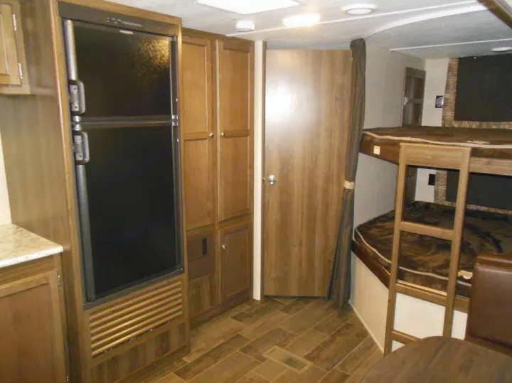 RV rental interior showcasing a large fridge, ample cabinets, and cozy bunk beds with ladder. Ideal for family travel.. Keystone RV Bullet Ultra Lite 2017