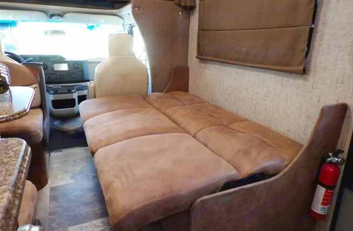 RV rental interior: driver's cab, a plush sofa bed, and side kitchen counter with patterned flooring.. Coachmen Leprechaun 2018