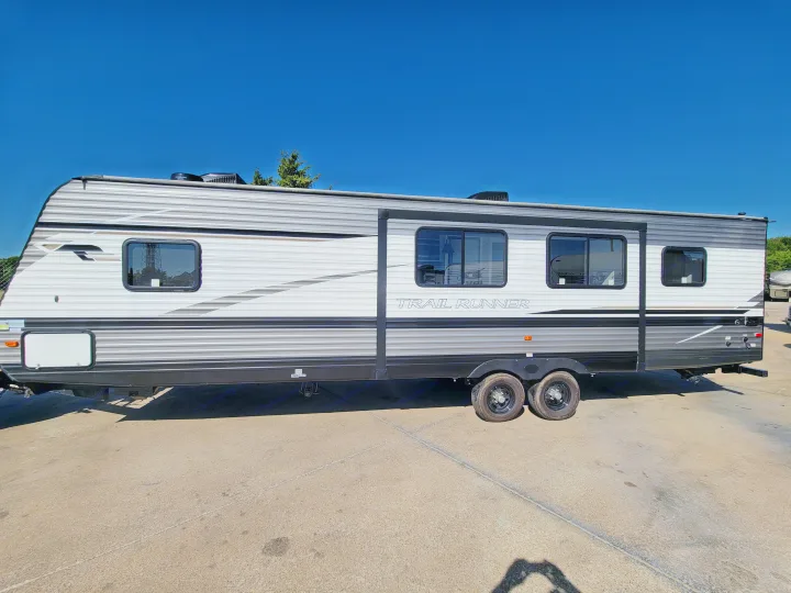 A sleek grey and white Trail Runner travel trailer, ready for an RV rental adventure, parked on asphalt under clear blue sky.. Heartland Trail Runner 2020