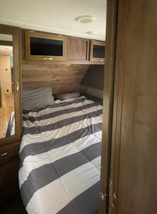 Comfortable RV rental bedroom featuring a striped bed, mounted TV, and overhead storage for your road trip comfort.. Dutchmen Coleman Light LX 2018