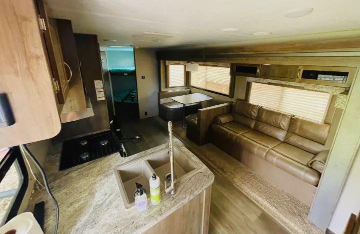 Explore this bright RV rental interior: a full kitchen with sink/stove, dining booth, comfy sofa, and bunk beds in the rear.. Dutchmen Coleman Light LX 2018