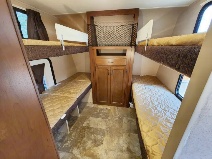 Inside this **rv rental**, four cozy bunk beds with quilted toppers and a central cabinet offer practical sleeping space.. Jayco Jay Feather Ultra Lite 2015