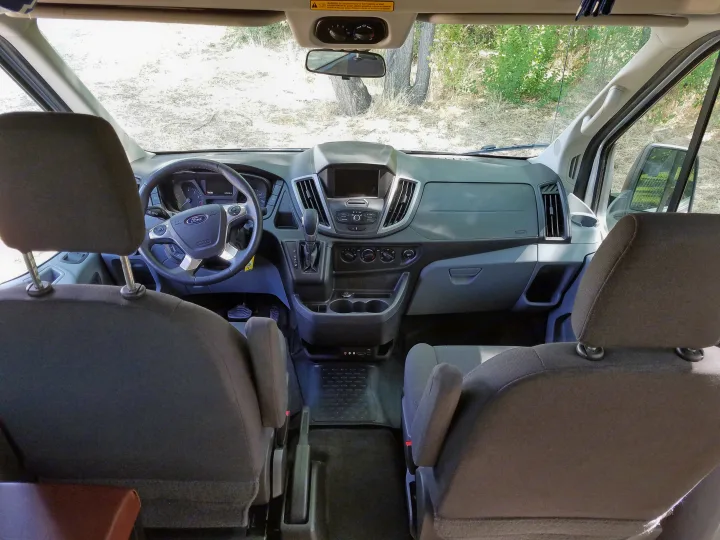 Inside an RV rental, this Ford van's front cabin features the dashboard, steering wheel, and seating.. Ford Transit 2017