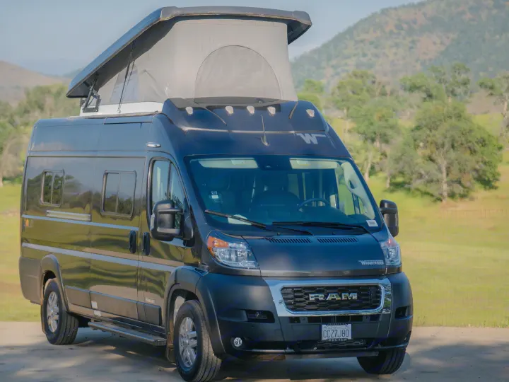 An rv rental: a dark Winnebago Solis camper van with pop-top extended, parked in a scenic outdoor setting.. Winnebago Solis 59PX 2023