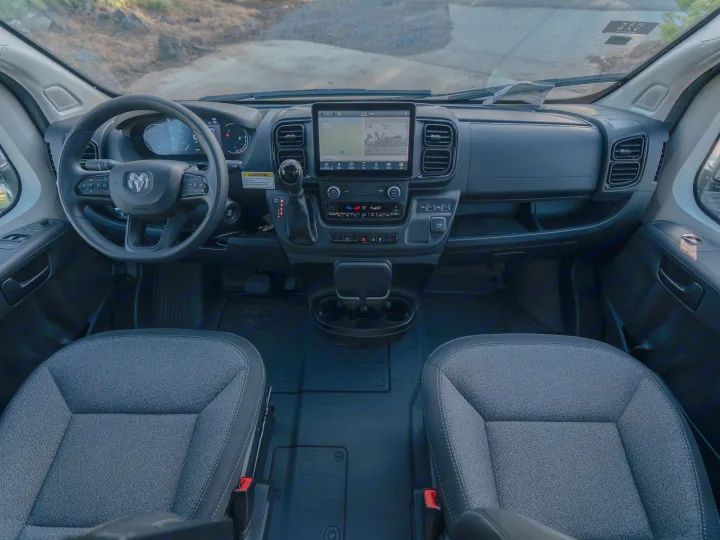 Interior view of an RV rental van's cockpit, featuring the modern dashboard, infotainment screen, and front seats.. Winnebago Solis 59PX 2023