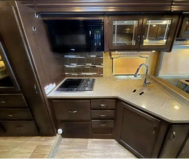 Modern RV rental kitchen featuring dark wood cabinets, microwave, cooktop, and sink.. Thor Motor Coach Four Winds 2018