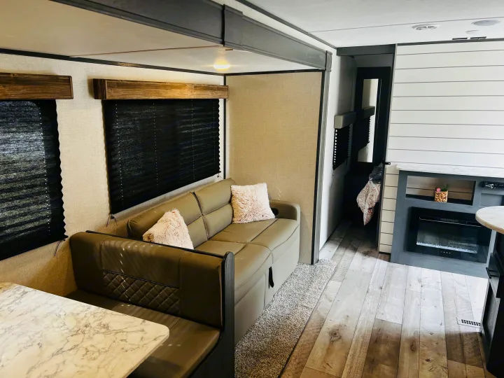 RV rental living space with a modern sectional sofa, marble-look dinette, and electric fireplace.. Dutchmen Aspen Trail LE 2023