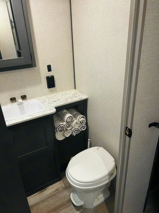 Compact rv rental bathroom featuring a sink, black vanity with rolled towels, and a white toilet.. Dutchmen Aspen Trail LE 2023
