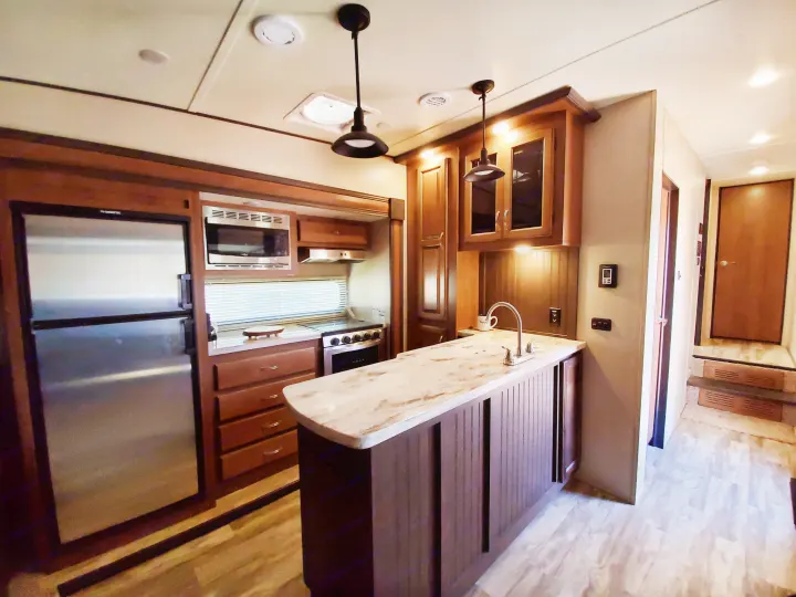 RV rental: Modern kitchen interior with fridge, microwave, stove, and island sink. Features wood cabinets and light flooring.. Forest River Coachmen Chaparral Lite 2020
