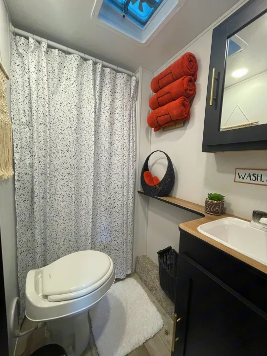 Stylish RV rental bathroom with a white toilet, speckled shower curtain, modern black vanity, and orange towels.. Keystone Springdale 2022