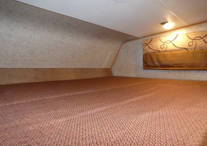 Cozy RV rental over-cab bed with brown mattress, patterned walls, and a window blind. Ideal camper sleeping space.. Coachmen Leprechaun 2018
