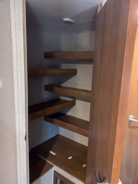 An RV rental's pantry featuring neatly organized, staggered wooden shelves for efficient storage.. Coachmen Apex 2016