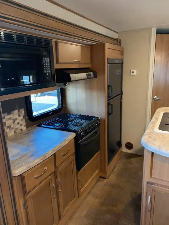 Well-equipped RV rental kitchen: Features a microwave, gas stove, fridge, and ample wood cabinets for your journey.. Coachmen Apex 2016