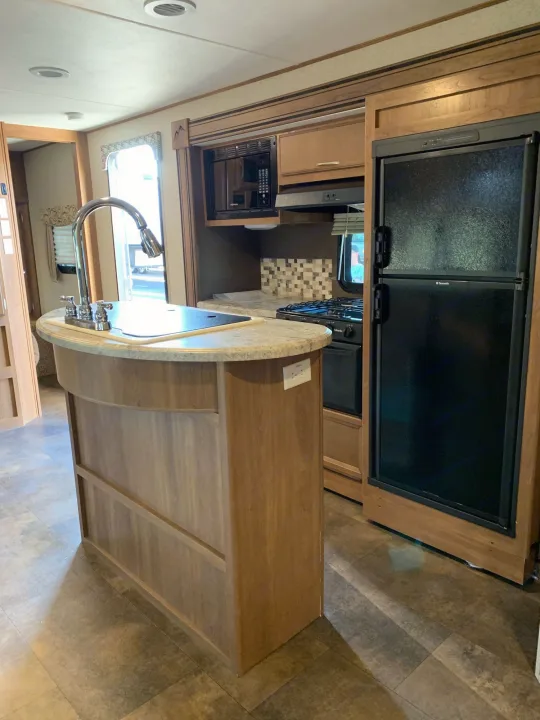 Spacious RV rental kitchen featuring a modern island, full-size refrigerator, and microwave, ideal for travel adventures.. Coachmen Apex 2016