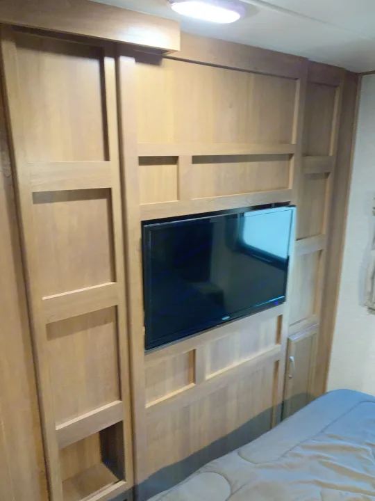 RV rental bedroom featuring a built-in entertainment center with a TV and ample wood-paneled storage.. Coachmen Apex 2016