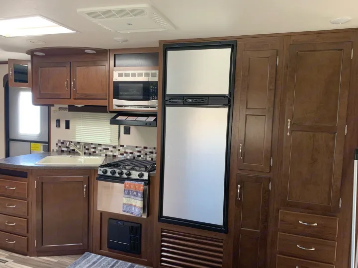 Compact RV rental kitchen features a fridge, microwave, stove, sink, and ample wood cabinets for efficient travel living.. Jayco Jay Flight 2017