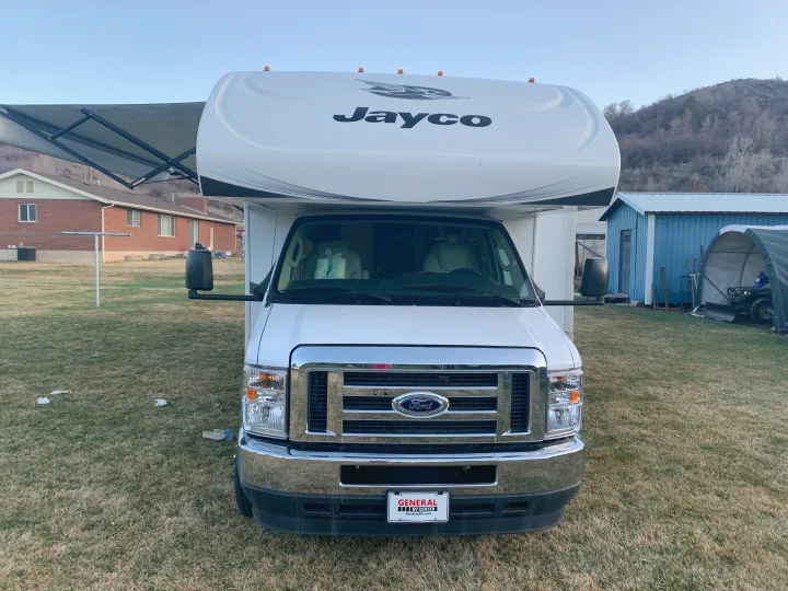Front view of a white Jayco rv rental motorhome, parked on grass with its awning extended for outdoor adventures.. Jayco Redhawk 2021