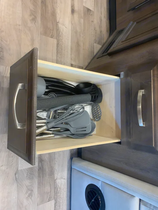 RV rental kitchen drawer open, filled with gray cooking utensils including spatulas, whisks, and a ladle.. Jayco Redhawk 2021