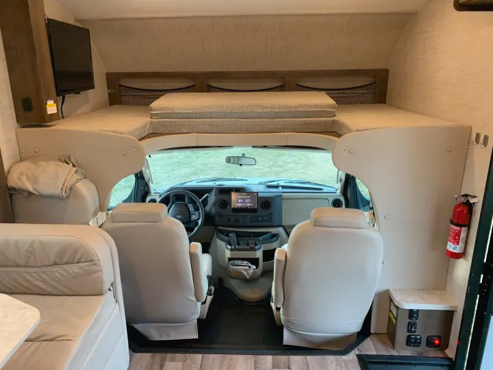 Spacious rv rental interior, featuring an over-cab bunk bed, front cockpit with dashboard, and main living area.. Jayco Redhawk 2021